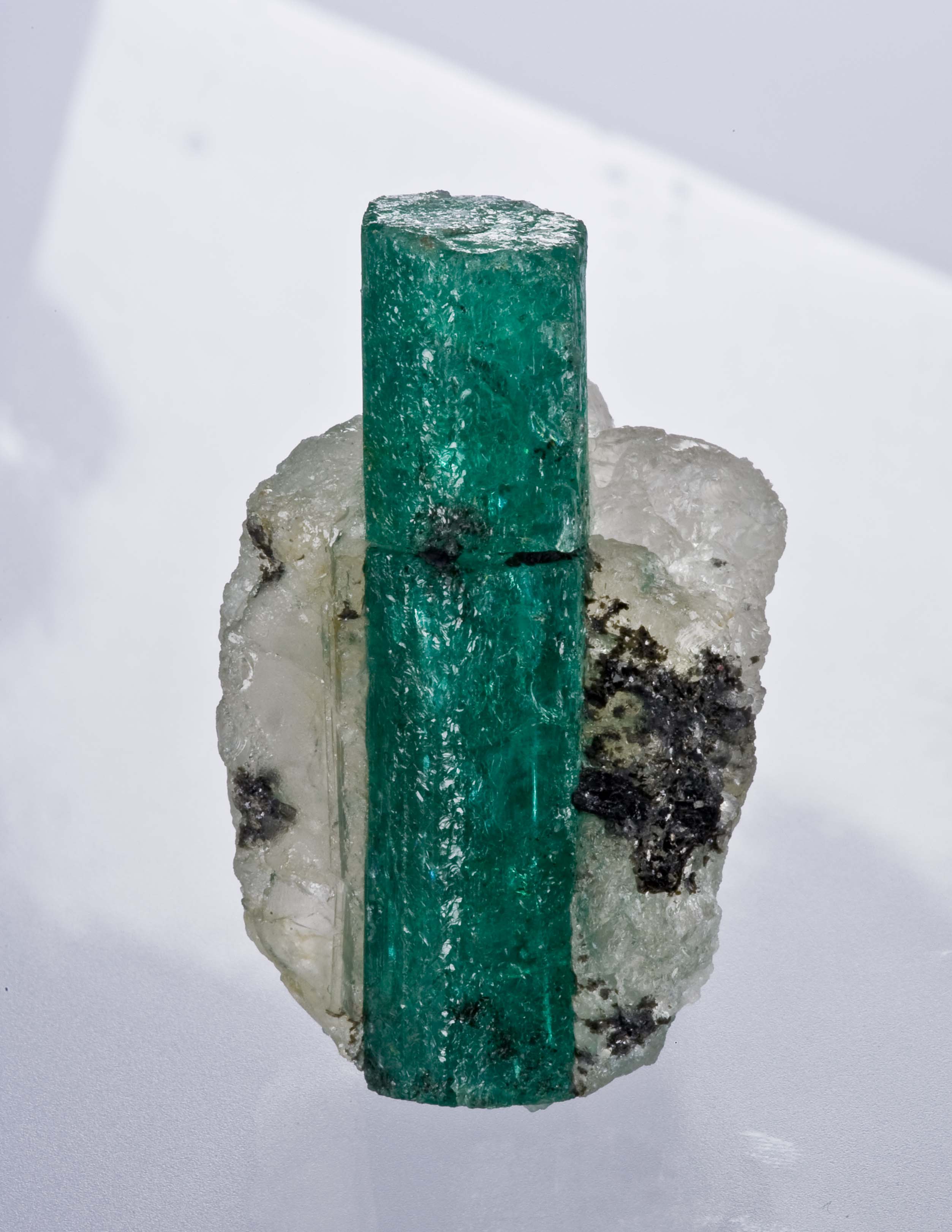 A green emerald crystal standing in white quartz.
