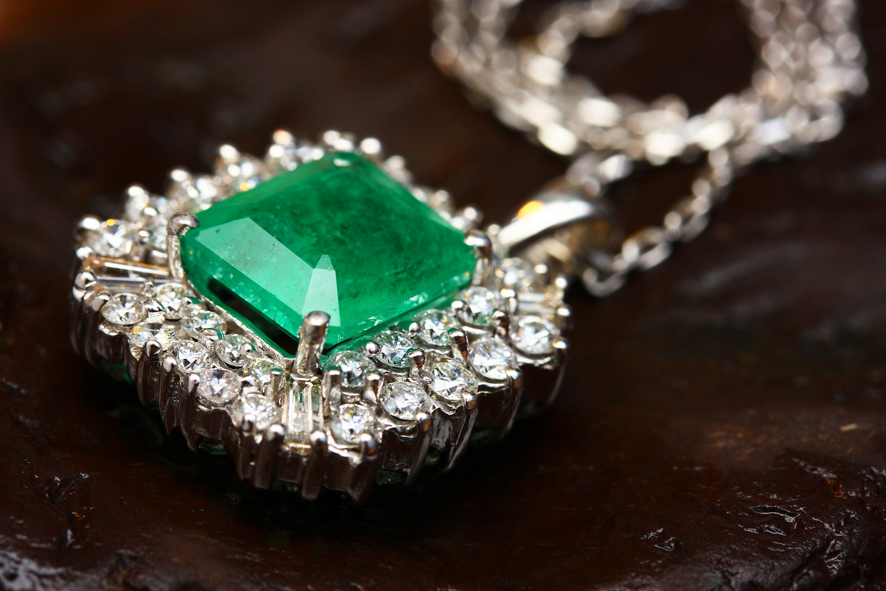 An emerald-cut green stone in a diamond halo pendant.