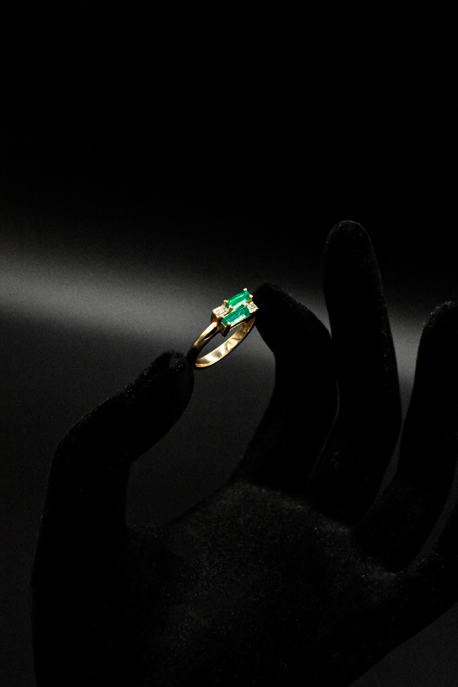A display hand holding a gold ring with green stones.