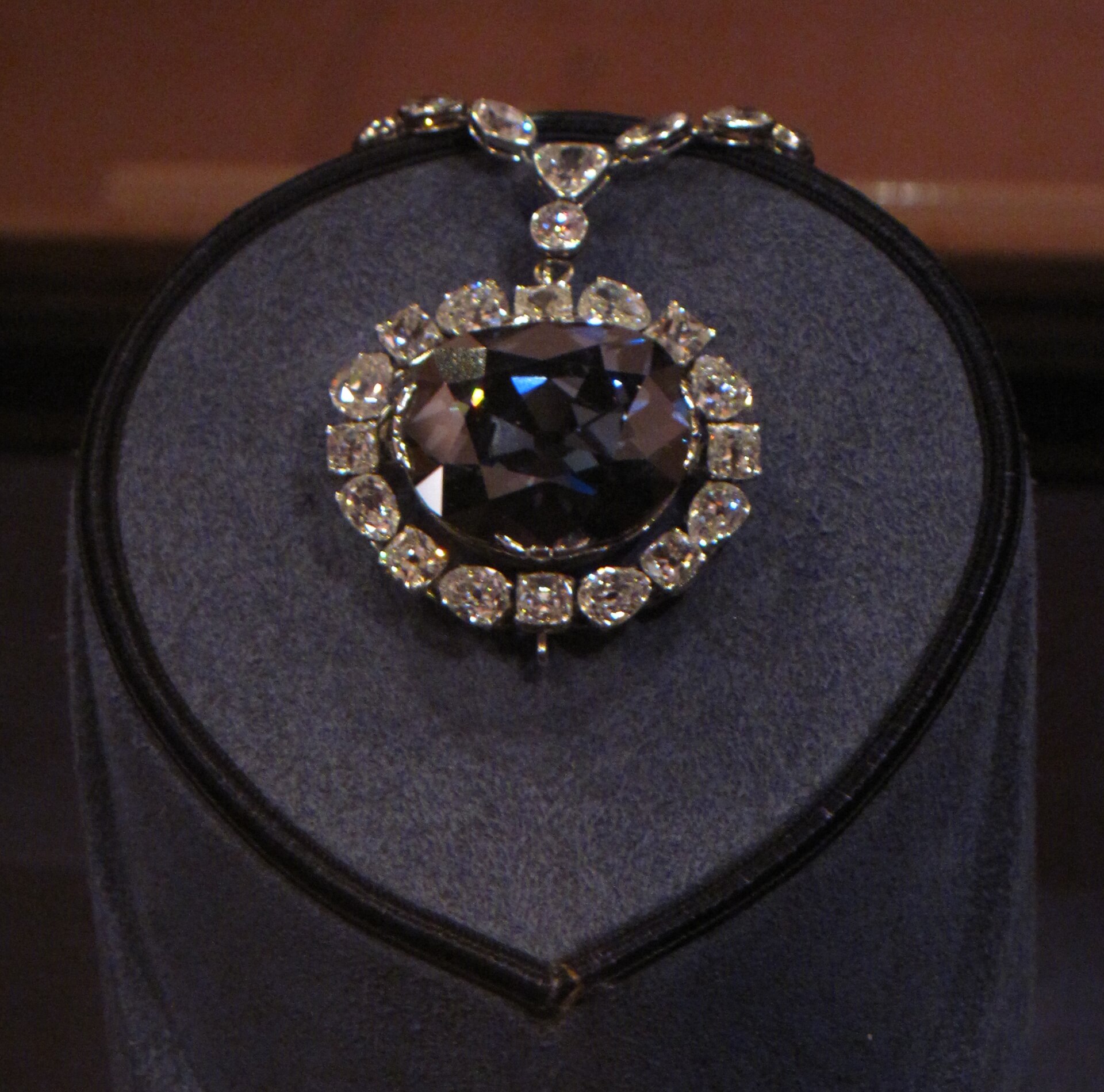 The Hope Diamond, a large deep blue diamond in a diamond-set pendant, displayed on a gray velvet stand.