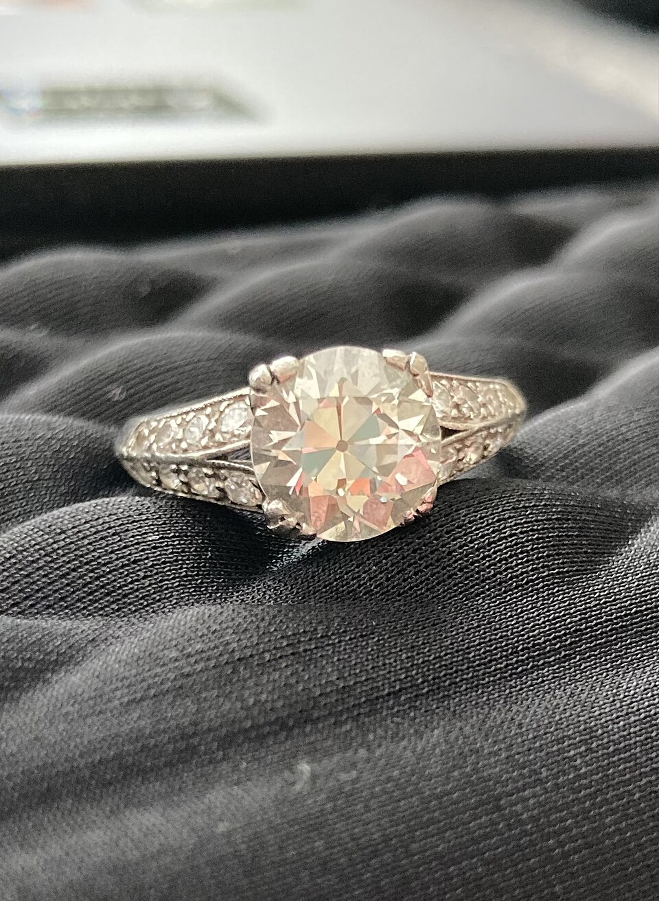 An old European cut diamond in a vintage white-metal ring on dark fabric.