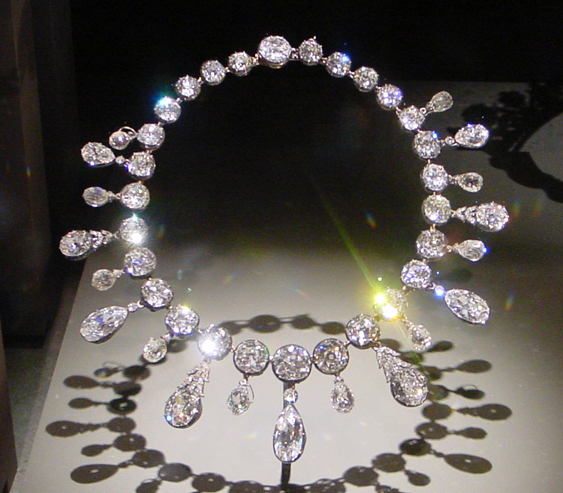 A diamond necklace of round stones and pear-shaped drops on a museum stand.
