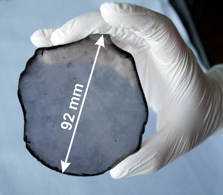 A gloved hand holding a dark round diamond wafer.